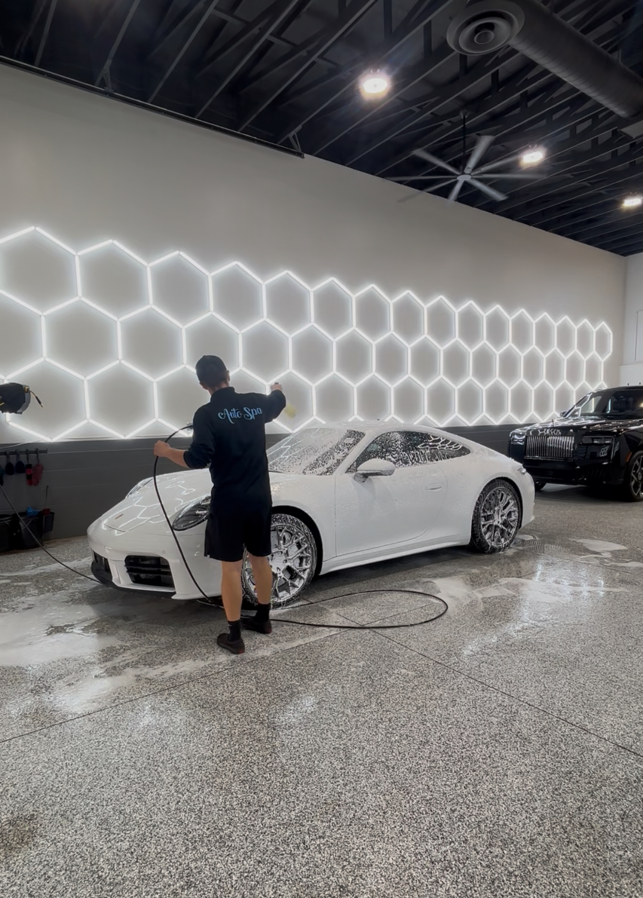 Auto Spa technician detailing a Porsche 911 in professional shop with hexagonal lighting